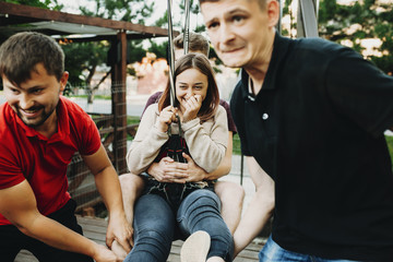 Lovely young caucasian girl showing a frightened face embraced by her boyfriend while is pulled by other two man for making speed on the rope slide.