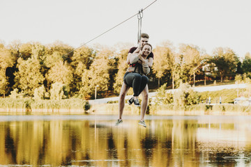 Lovely young couple smiling with closed eyes while zip lining on a rope slide above the lake.