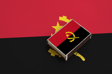 Angola flag  is pictured on a matchbox that lies on a large flag