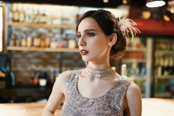 Close-up portrait of a young attractive woman in a 1920s style at the bar. Model with a beautiful...