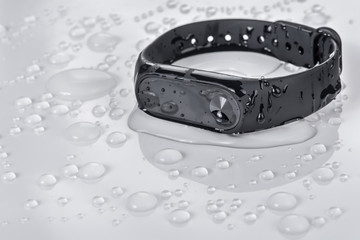 Fitness bracelet on a white glossy background with drops of water