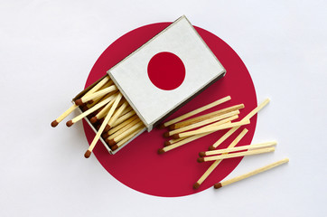 Japan flag  is shown on an open matchbox, from which several matches fall and lies on a large flag