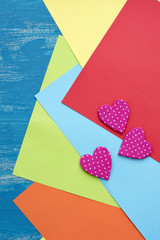 Colored sheets of paper on a wooden painted blue background decorative heart Valentine's day.