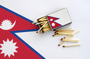 Nepal flag  is shown on an open matchbox, from which several matches fall and lies on a large flag