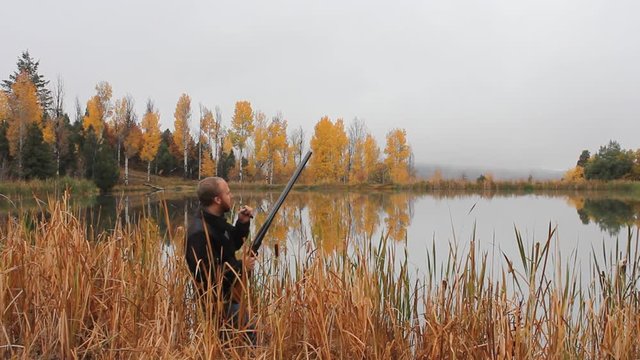Duck hunter stands in the reeds next to a pond waiting and calling for the ducks. Misty foggy morning, perfect for hunting.