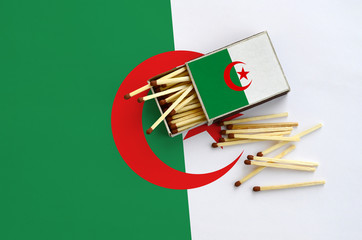 Algeria flag  is shown on an open matchbox, from which several matches fall and lies on a large flag