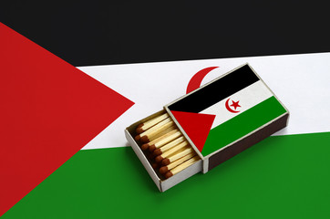 Western Sahara flag  is shown in an open matchbox, which is filled with matches and lies on a large...