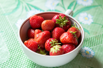 ripe strawberry berry with green leafs in a plate on a green background