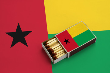 Guinea Bissau flag  is shown in an open matchbox, which is filled with matches and lies on a large...