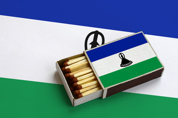 Lesotho flag  is shown in an open matchbox, which is filled with matches and lies on a large flag
