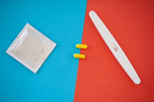 Pregnancy test. The result is positive with two strips and condom with contraceptive on colored background, Birth control pill, safe sex, healthcare concep