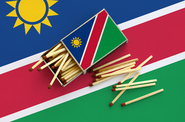 Namibia flag  is shown on an open matchbox, from which several matches fall and lies on a large flag