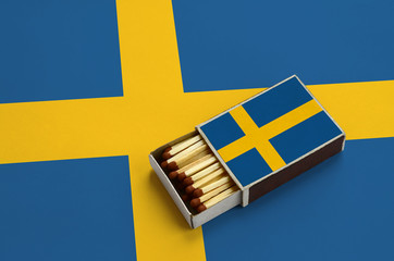 Sweden flag  is shown in an open matchbox, which is filled with matches and lies on a large flag