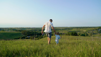 Naklejka na ściany i meble Father and daughter share love walking together in high grass field. Young caucasian happy father have leisure time with toddler daughter. Confidence in future. Parenthood, childhood, healthy concept