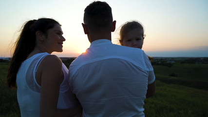 Pregnant couple with toddler daughter have leisure time outdoors at sunset. Happy young parents with child at sunset. Father holding kid. Parenthood, pregnancy, childhood, healthy, activity concept