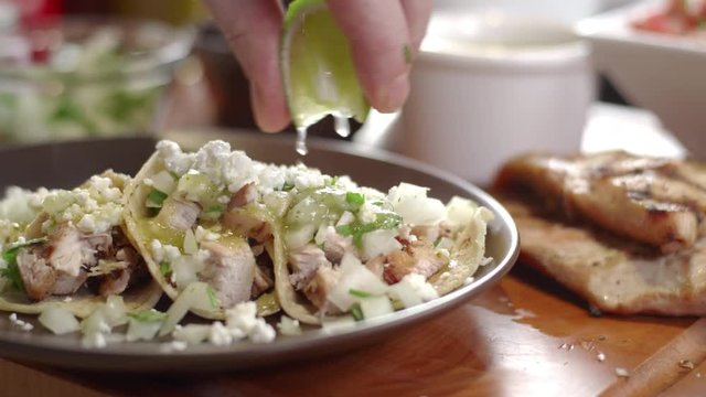 Slow-motion shot of fresh lime juice squeezed over plate of steaming tacos