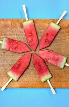 Sweet fresh dessert,watermelon and fruity concept:  sliced watermelon with sticks on a wooden board and a blue background.