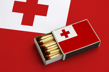 Tonga flag  is shown in an open matchbox, which is filled with matches and lies on a large flag