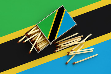 Tanzania flag  is shown on an open matchbox, from which several matches fall and lies on a large...