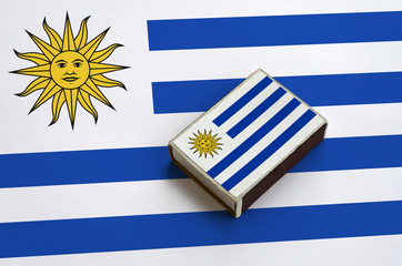Uruguay flag  is pictured on a matchbox that lies on a large flag