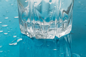 Glass of cold water with drops and reflection in blue surface. Drink of health freshness aqua concept