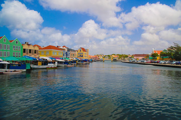 Obraz premium A view on the blue sea and many very colorful caribbean houses. Also there are some also colorful boats docking next to the houses. Furthermore there is a blue and white sky with some clouds.