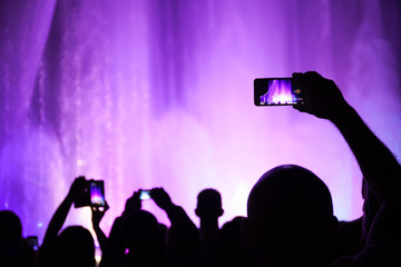 People shoot photos or video of a concert or lighting show on smartphones.