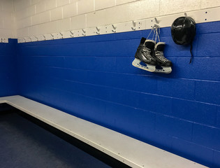 Hockey skates and helmet hanging in locker room with blue background and copy space  