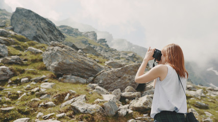 Naklejka premium A young woman hiker walks in the mountains with photo camera. Transfagarasan, Carpathian mountains in Romania