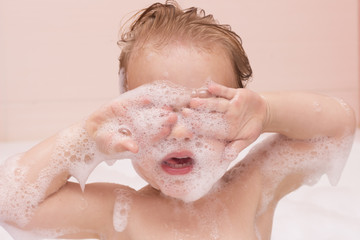 Baby boy rubbing eyes in bath tub. Infant kid in a foam. Close-up portrait. Cute toddler with closed eyes