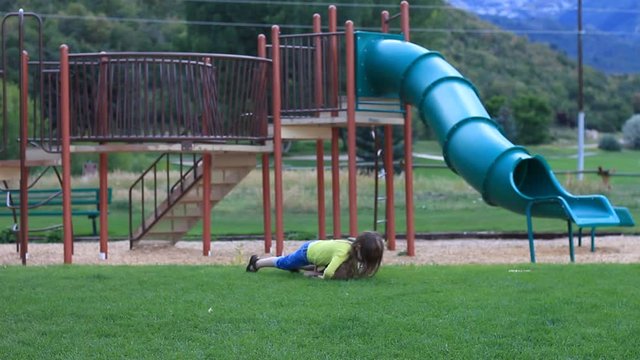 Mean little bully girl pushes and wrestles a smaller boy to the ground at the playground.