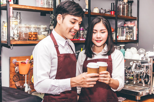 Portrait of couple small business owner smiling and holding coffee behind the counter bar in a cafe.Couple barista giving coffee cup to customer at cafe