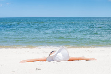 Fototapeta na wymiar Tanned beautiful woman in hat lying on the beach sand