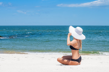 Fototapeta na wymiar Beautiful woman in bikini and hat sitting on the beach enjoying summer holidays