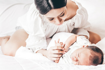 Mother holding sleeping baby hand on white bed.Love of family concept