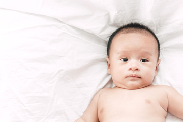 Portrait of baby relaxing on white bed in room