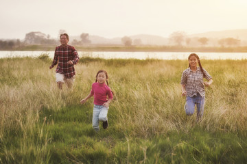happy family of three people, father and child running in front of a sunset sky.