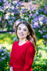 Beautiful young woman in a red sweater in the park near the lilac blossom.