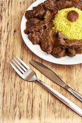 Plate with meat and liver under sauce with rice and plate with soup with fork, knife and spoon on wooden table