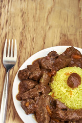 Plate with meat and liver under sauce with rice and plate with soup with fork, knife and spoon on wooden table