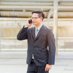 Young Asia handsome businessman with his smartphone standing on walkway of modern city.