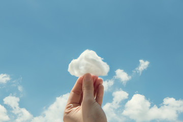Woman hand holding cotton wool on cloud sky background. The development of the imagination, copy...