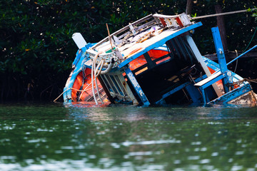 Obraz premium Fishing boat that sank in the sea with a forest background.