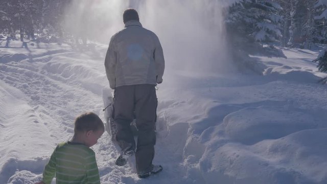Little boy watching daddy use the snowblower