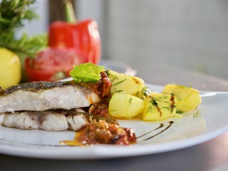 Dish of prepared potatoes with herbs and fish on white plate.