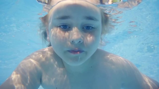 Close up shot of a little girl floating under the water looking forward.