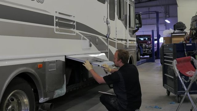Man repairing a large RV in a body shop. 