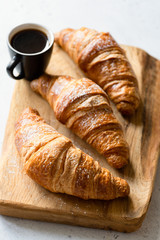 Croissants and coffee on wooden board. Freshly baked croissants. French croissant and cup of black coffee espresso. Selective focus