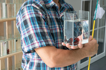 Asian male showing glass jar of siamese fighting or betta fish. Man holding glass jar and small nylon scoop fish for selling or bidding.