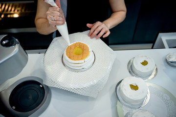 Asian women is confectionery bag squeezing tea cream on cupcakes, a rounded cakes for welcoming people to the evening party.